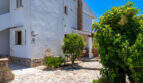 Weißes Erdgeschossapartment in Cala Murada mit Natursteinpflaster, üppigem Grün und überdachter Terrasse.