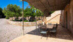 Überdachte Terrasse mit Esstisch aus Schmiedeeisen, Natursteinmauer und Orangenbäumen auf Finca in Mallorca.