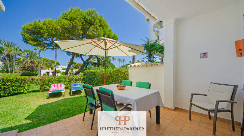 Sonnige Terrasse mit Esstisch und Sonnenschirm, Blick auf gepflegten Garten mit Liegestühlen, Cala d'Or
