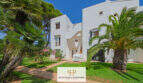 Außenansicht weißer Apartmentanlage in Cala d'Or mit Palmen, gepflegtem Rasen und mediteraner Bepflanzung.