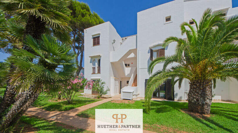 Außenansicht weißer Apartmentanlage in Cala d'Or mit Palmen, gepflegtem Rasen und mediteraner Bepflanzung.
