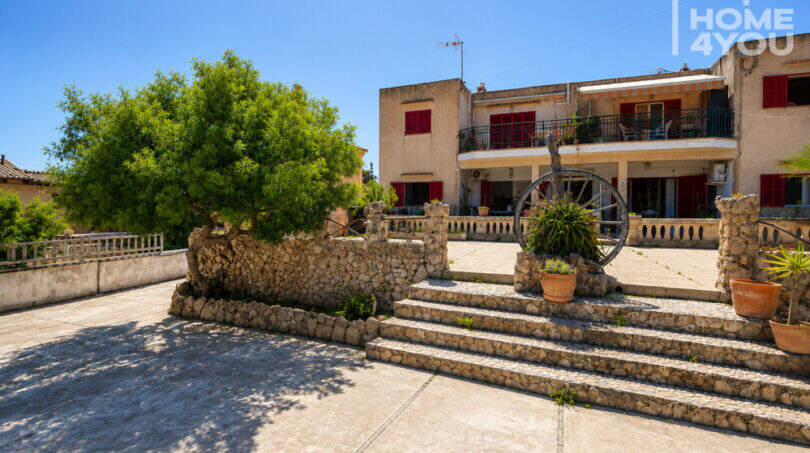 Außenansicht der Erdgeschosswohnung in Cala Llombards mit gepflastertem Vorplatz, Steinmauer und üppigem Baum.
