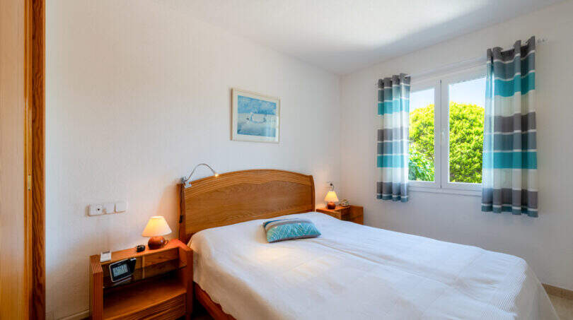 Helles Schlafzimmer mit Doppelbett, Holzmöbeln und türkisen Vorhängen in Doppelhaus Cala Murada