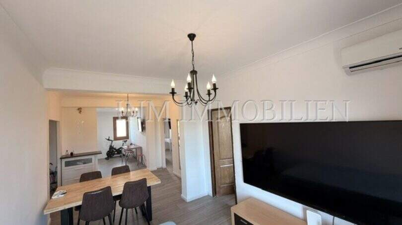Luminoso salón con gran televisor, mesa de comedor y lámpara de araña en apartamento renovado en Palma