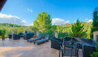 Weitläufige Terrasse der Finca Son Macià mit Loungemöbeln, Sonnenliegen und Blick auf grüne Hügel.