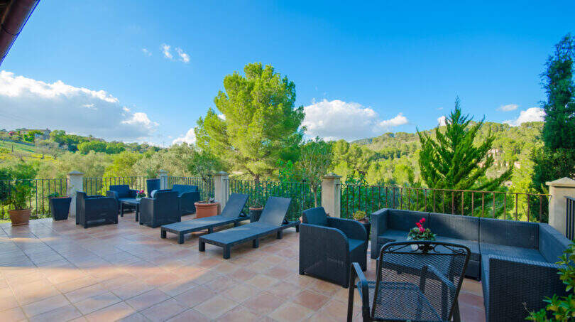 Weitläufige Terrasse der Finca Son Macià mit Loungemöbeln, Sonnenliegen und Blick auf grüne Hügel.
