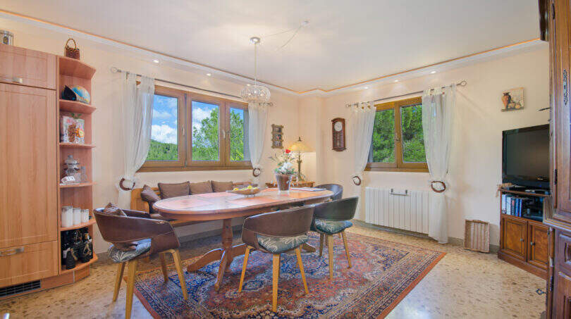 Helles Esszimmer der Finca Son Macià mit ovalem Holztisch, Orientteppich und großen Fenstern mit Gartenblick.