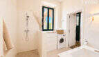 Helles Badezimmer mit Regendusche, Waschmaschine und grünem Fenster in historischer Wohnung Ses Salines