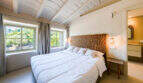 Helles Schlafzimmer der Finca Esporles mit Holzkopfteil, Gewölbedecke und Fenster mit Gartenblick.