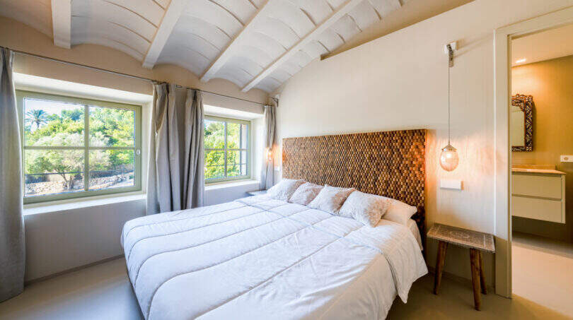Helles Schlafzimmer der Finca Esporles mit Holzkopfteil, Gewölbedecke und Fenster mit Gartenblick.