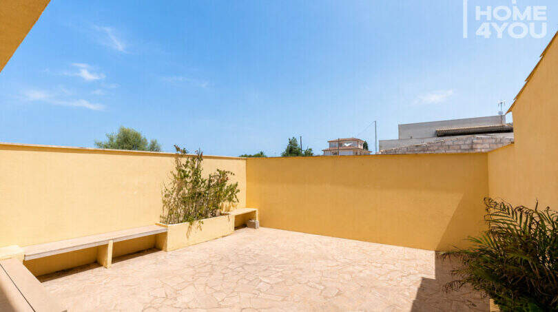 Sonnige Dachterrasse mit Natursteinboden, gelben Mauern und Bepflanzung des Eckreihenhauses in Ses Salines.
