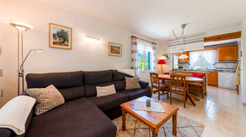 Helles Wohnzimmer mit dunklem Sofa, Holztisch und offener Küche im Doppelhaus Cala Murada