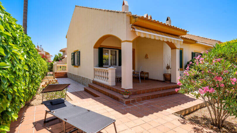 Außenansicht Doppelhaus Cala Murada mit überdachter Terrasse, Liegestühlen und gepflegtem Garten mit Oleander.