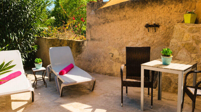 Sonnige Terrasse des Agroturismo mit Liegestühlen, Rattanmöbeln, Sonnensegel und historischer Steinmauer bei Ses Salines