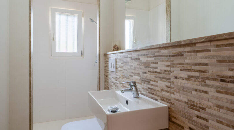 Cuarto de baño moderno de la villa de Cala Murada, con azulejos de mosaico, lavabo sobre encimera y zona de ducha.