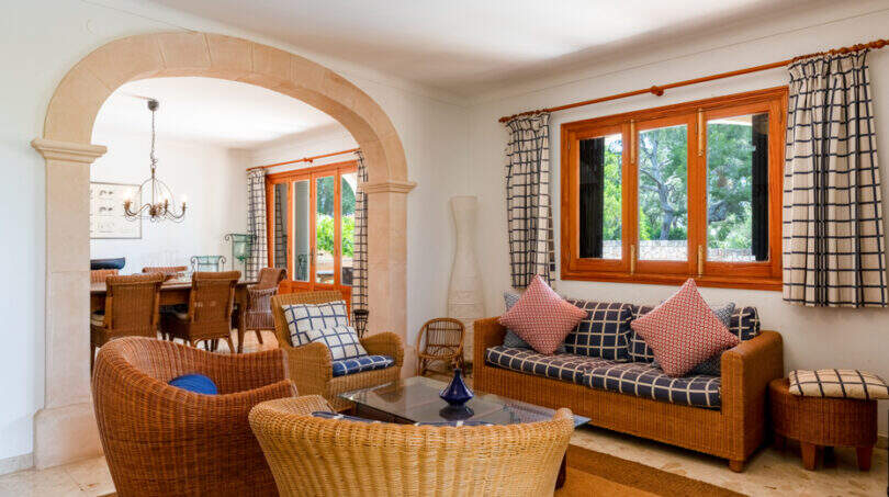 Luminoso salón de la villa familiar de Cala Murada, con muebles de ratán, un arco de medio punto y vistas al comedor.
