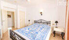 Helles Schlafzimmer mit Doppelbett, schwarzem Metallrahmen, blauer Bettwäsche, Deckenventilator und weißen Nachttischen.