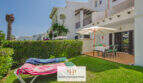 Sonnige Terrasse mit Esstisch und Sonnenschirm, Liegestühlen auf gepflegtem Rasen, weiße mediterrane Fassade, Cala d'Or