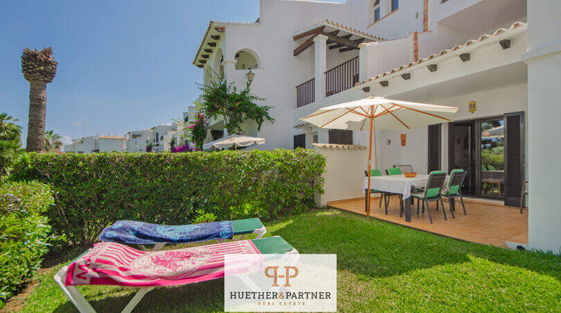 Sonnige Terrasse mit Esstisch und Sonnenschirm, Liegestühlen auf gepflegtem Rasen, weiße mediterrane Fassade, Cala d'Or
