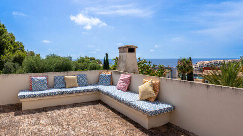 Terraza en la azotea con un banco en forma de L, cojines de colores y vistas al mar en Villa Cala Murada
