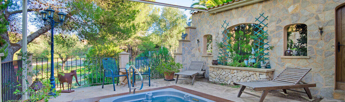 Sonnige Terrasse der Finca Son Macià mit eingelassenem Jacuzzi, Natursteinmauer und Liegestühlen