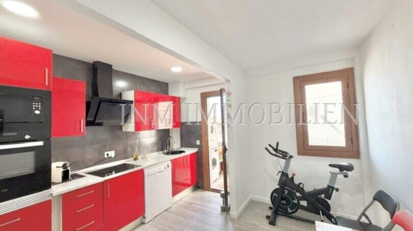 Cocina moderna con frentes rojos de alto brillo, electrodomésticos integrados y área deportiva en apartamento renovado en Palma