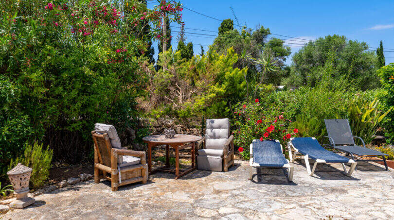 Sonnenterrasse mit Liegestühlen und Sitzgruppe, umgeben von üppigem mediterranem Garten in Cala Murada.