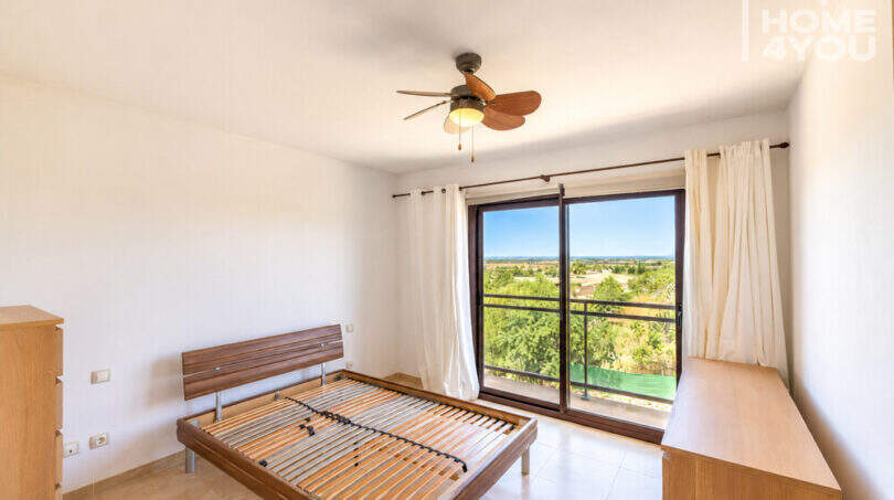Helles Schlafzimmer mit Holzbett, Deckenventilator und Balkon mit Meerblick im Eckreihenhaus Ses Salines