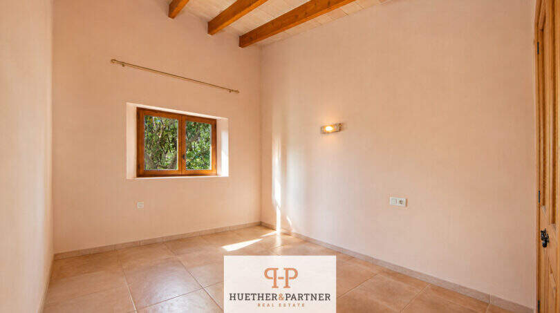Helles leeres Zimmer der Finca Felanitx mit Holzbalkendecke, Terrakottaboden und kleinem Holzfenster zum Garten