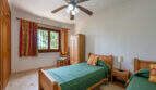 Dormitorio de la villa de Cala Murada con dos camas individuales, muebles de madera y ventilador de techo.