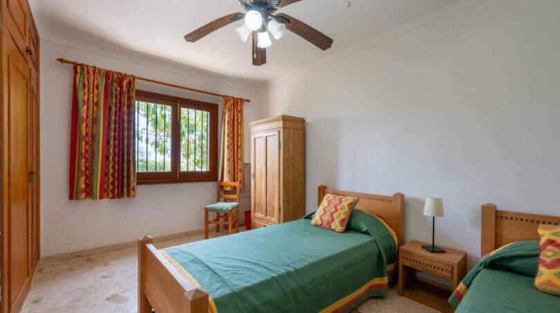 Dormitorio de la villa de Cala Murada con dos camas individuales, muebles de madera y ventilador de techo.
