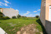 Urbanes Baugrundstück 391 m² in Ses Salines mit grüner Rasenfläche, Olivenbäumen und Nachbargebäuden unter blauem Himmel.