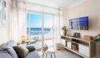 Luminosa sala de estar con balcón con vistas al mar, sofá y muebles para TV en apartamento en Port Adriano, Calvià
