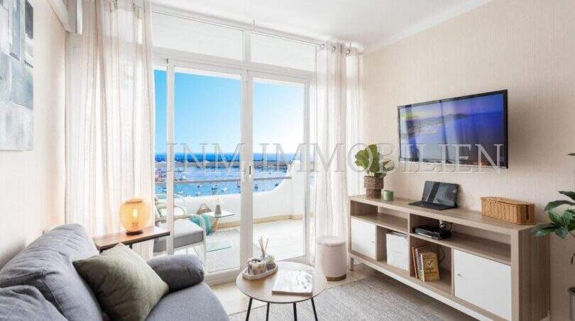 Luminosa sala de estar con balcón con vistas al mar, sofá y muebles para TV en apartamento en Port Adriano, Calvià