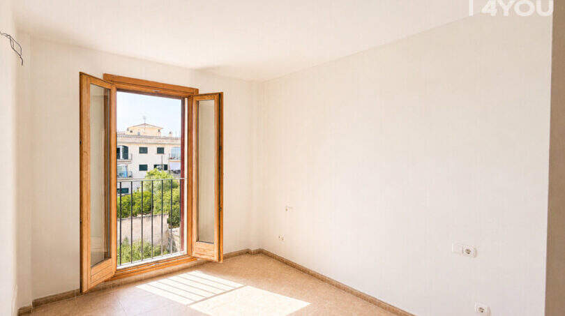 Helles leeres Schlafzimmer mit Fliesenboden und Holzbalkon-Tür, Blick auf Nachbargebäude in Llucmajor