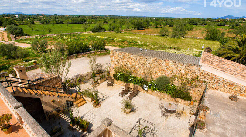 Luftaufnahme des Agroturismo: historischer Innenhof mit Sandsteinmauer, Loungemöbeln und Gartenanlage bei Ses Salines