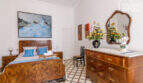 Schlafzimmer mit antikem Holzbett, Kommode mit Spiegel, Blumenstrauß und Gemälden im historischen Herrenhaus Porreres