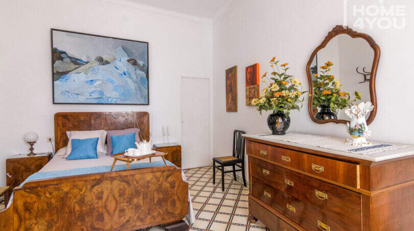 Schlafzimmer mit antikem Holzbett, Kommode mit Spiegel, Blumenstrauß und Gemälden im historischen Herrenhaus Porreres