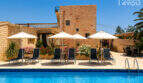 Pool mit Sonnenliegen und Sonnenschirmen vor historischem Sandsteingebäude des Agroturismo in Ses Salines