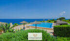 Infinity-Pool mit Meerblick, Strohdach-Sonnenschirme und gepflegte Gartenanlage einer Apartmentanlage in Cala d'Or.