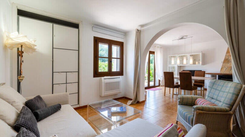 Helles Wohnzimmer mit weißem Sofa, Glastisch und Rundbogen zur Essdiele in Apartment Cala Murada