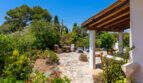 Natursteintetrasse mit Holzpergola und üppigem Garten unter blauem Himmel in Cala Murada