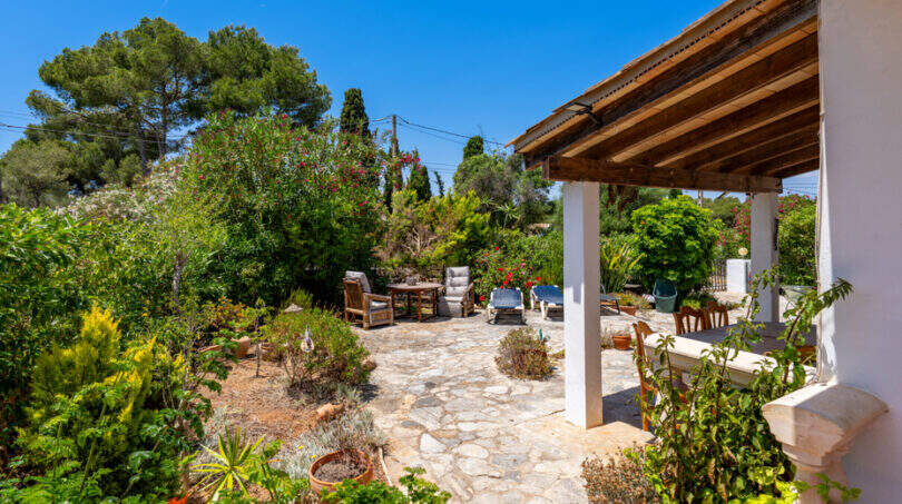 Natursteintetrasse mit Holzpergola und üppigem Garten unter blauem Himmel in Cala Murada