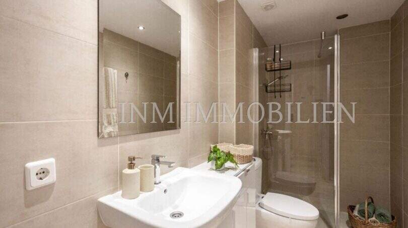 Cuarto de baño moderno del apartamento en primera línea de mar en Port Adriano con ducha, WC y decoración de azulejos beige claro.