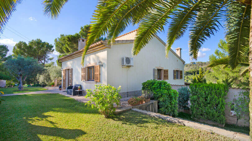Finca Son Macià: Mediterrane Villa mit Palmengarten, Holzläden und gepflegtem Rasen unter blauem Himmel.