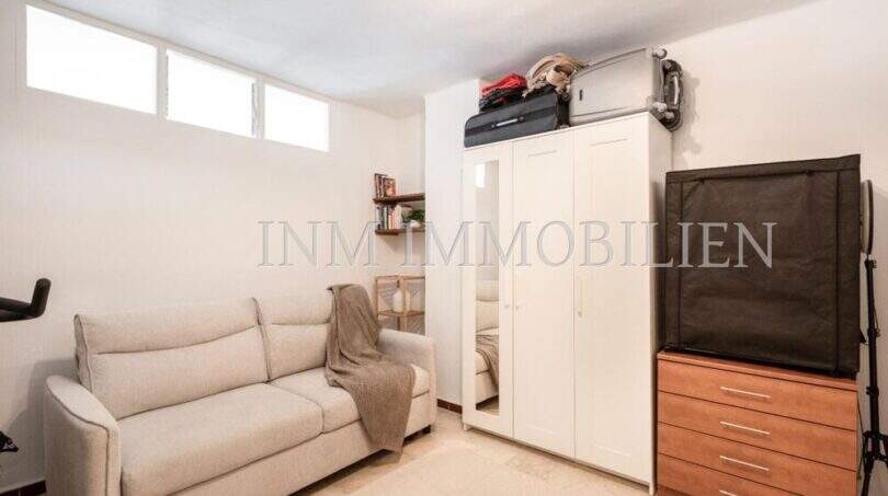 Dormitorio luminoso del apartamento en Port Adriano con sofá, armario blanco y cómoda