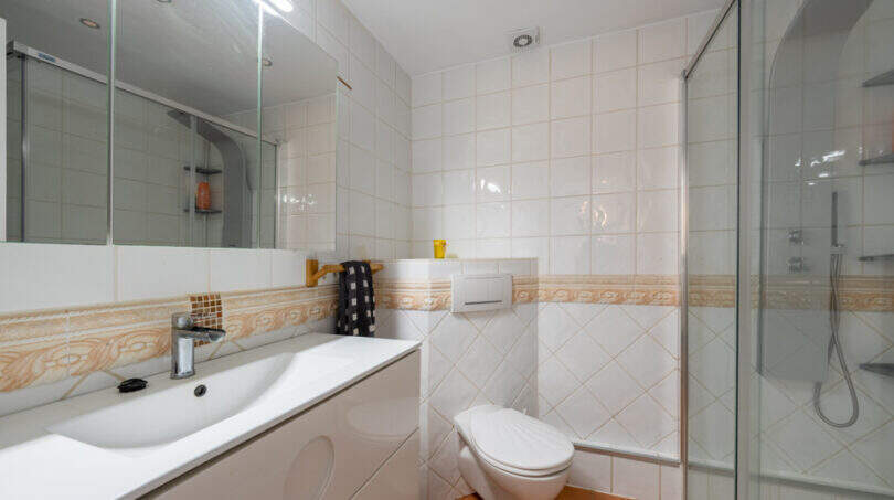Helles Badezimmer mit weißem Waschtisch, Duschkabine und WC, geflieste Wände mit Bordüre, Apartment Cala Murada