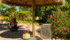 Gartenbereich mit Palapa-Sonnenschirm, Liegestuhl und Beistelltisch, umgeben von Palmen und blühenden Sträuchern.