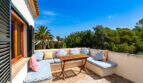 Terraza en la azotea soleada con un banco en forma de L, cojines de colores y una mesa de madera, rodeada de palmeras en Cala Murada