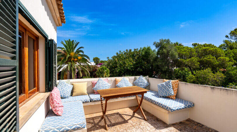 Terraza en la azotea soleada con un banco en forma de L, cojines de colores y una mesa de madera, rodeada de palmeras en Cala Murada